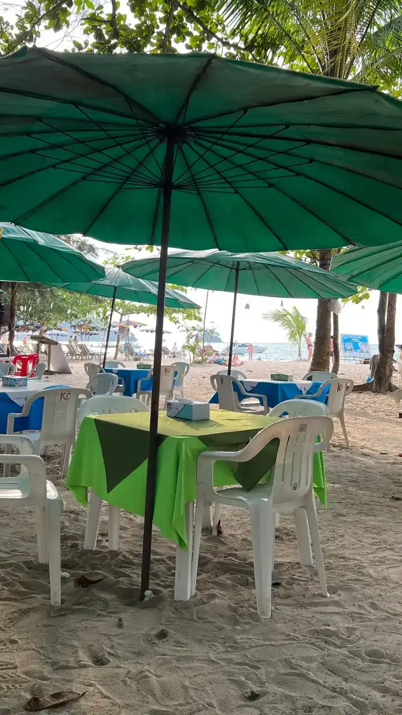 A table with a lime-green cloth and a darker cloth laid across it, under a green umbrella on the sand