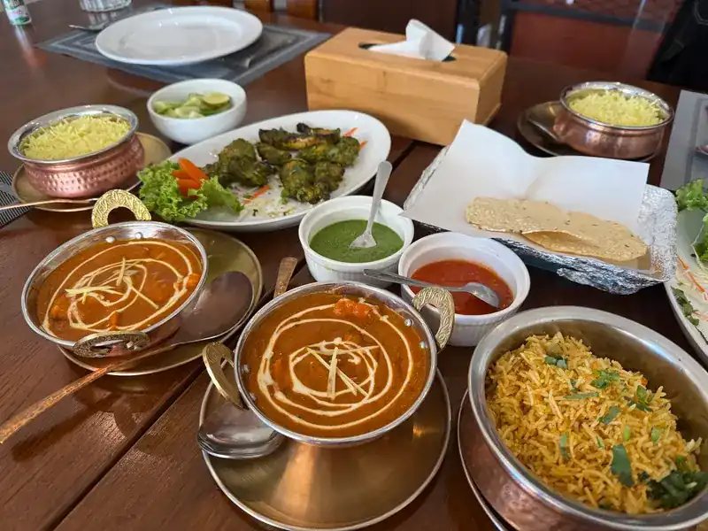 Curries in copper bowls, biryani, green tikka, pappadums and chutneys on a wooden table