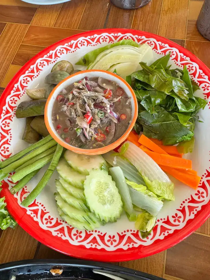 A bowl of chilli dip on a platter of cucumber, long beans, cabbage, carrot and fresh greens
