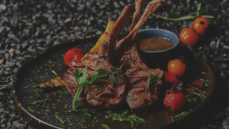 Grilled chops with roasted tomatoes and herbs on a dark plate