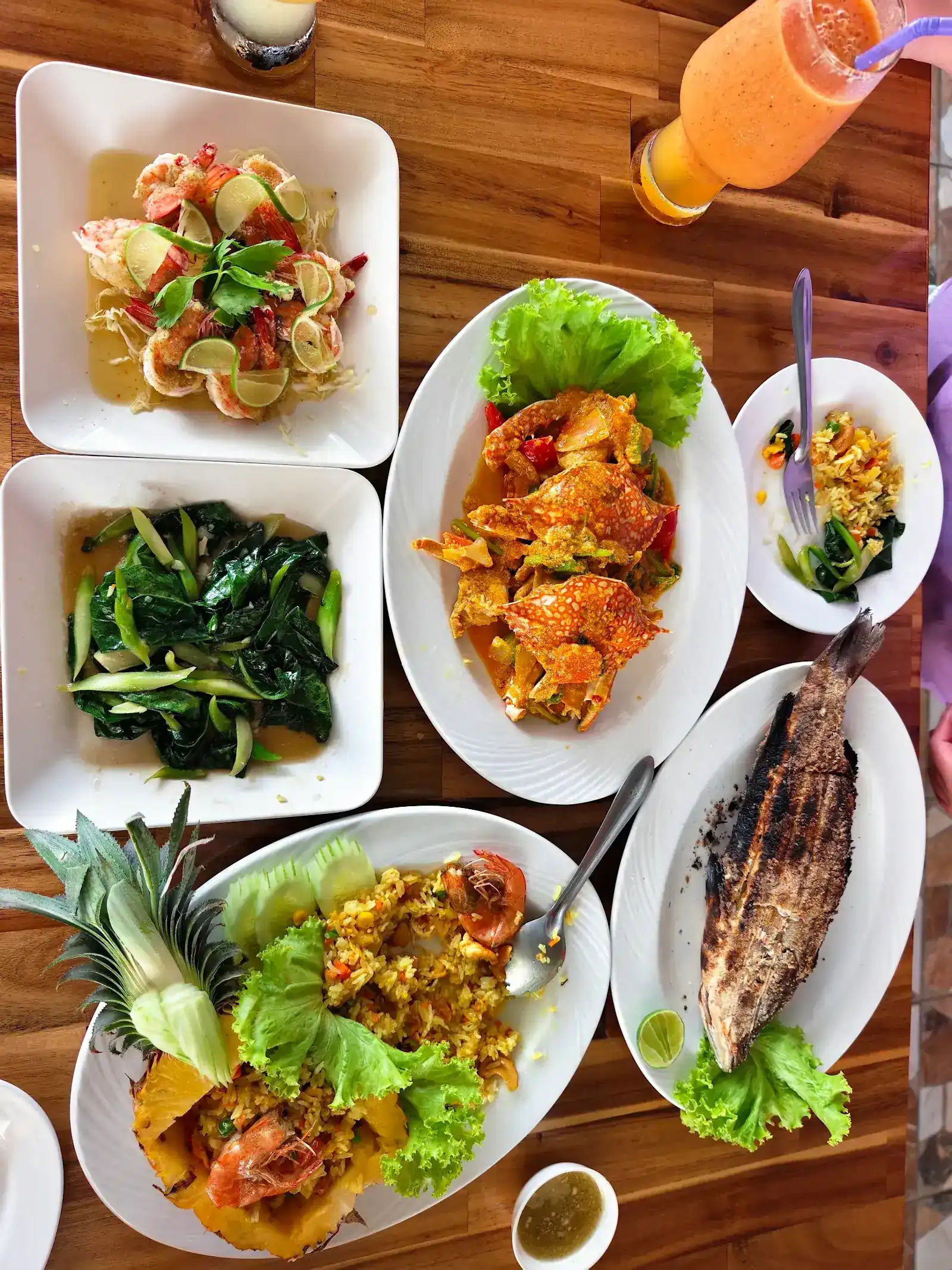 A table seen from above: crab in yellow curry, pineapple fried rice with prawns, a whole grilled fish, prawns with lime and stir-fried greens