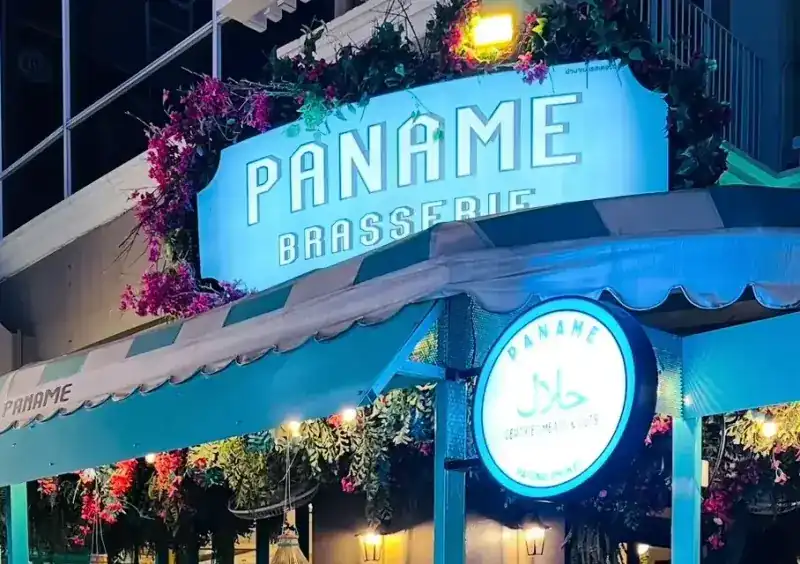 The lit PANAME Brasserie sign with bougainvillea above the striped awning, and the round halal sign