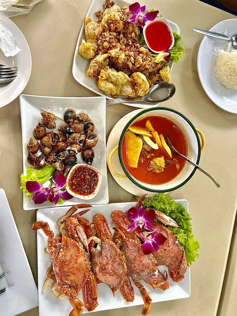A table seen from above: a crisp-fried dish with chilli sauce, spotted babylon with a dip, a bowl of curry and a plate of crabs