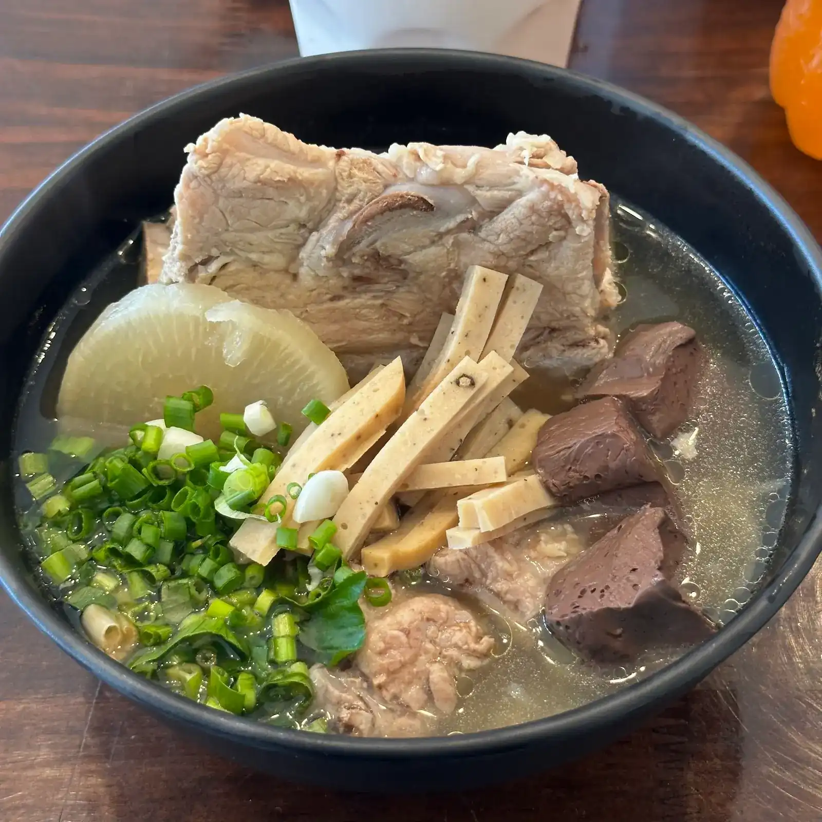 A bowl of kuay jap yuan with a large pork bone, radish, chicken sausage, blood and spring onion in clear broth