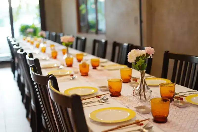 A long table laid for a party, with yellow plates, amber glasses and small vases of flowers