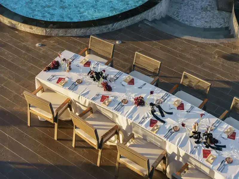 A long table set for a private dinner on the deck beside the pool, seen from above