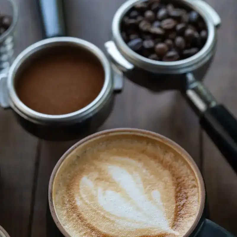 A latte beside portafilters of ground coffee and beans