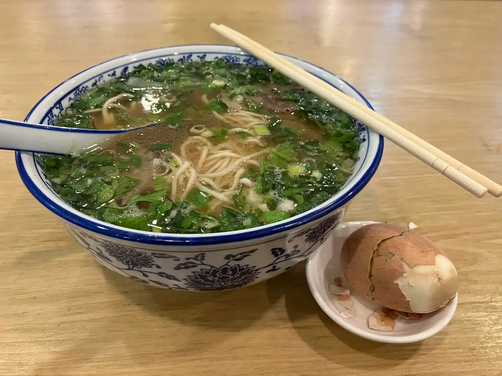 Beef noodle soup with coriander and spring onion in a blue-and-white bowl, a spiced egg on the side
