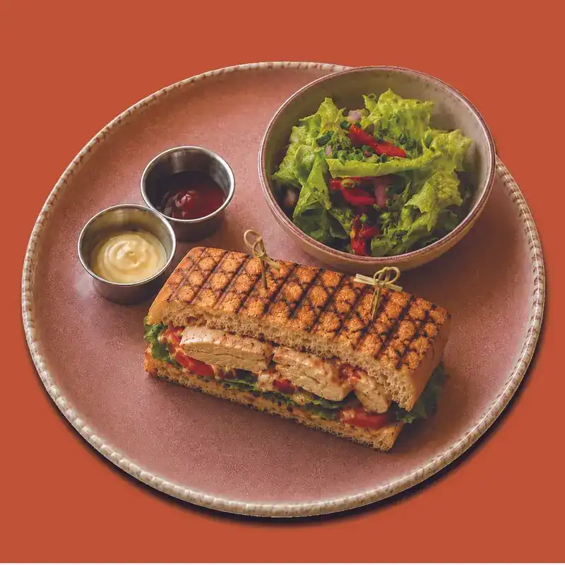 Grilled chicken sandwich held with picks, with salad and two dips