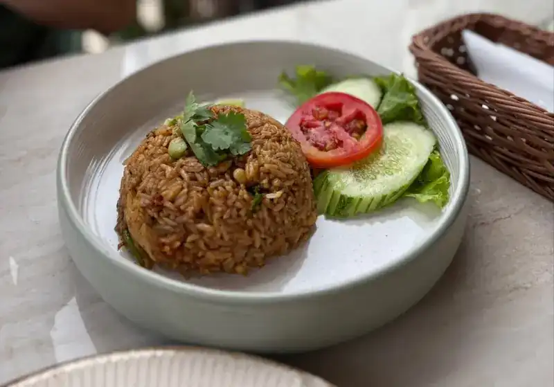 A dome of fried rice with tomato, cucumber and coriander in a pale bowl