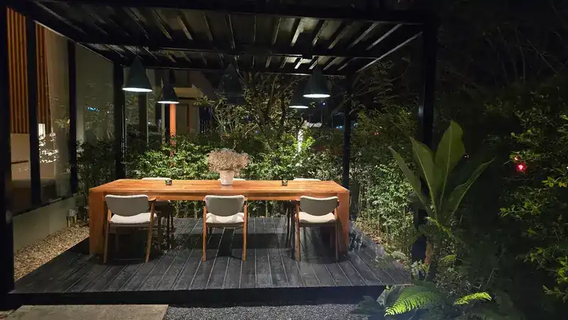 A long wooden table set in the garden at night under black pendant lamps