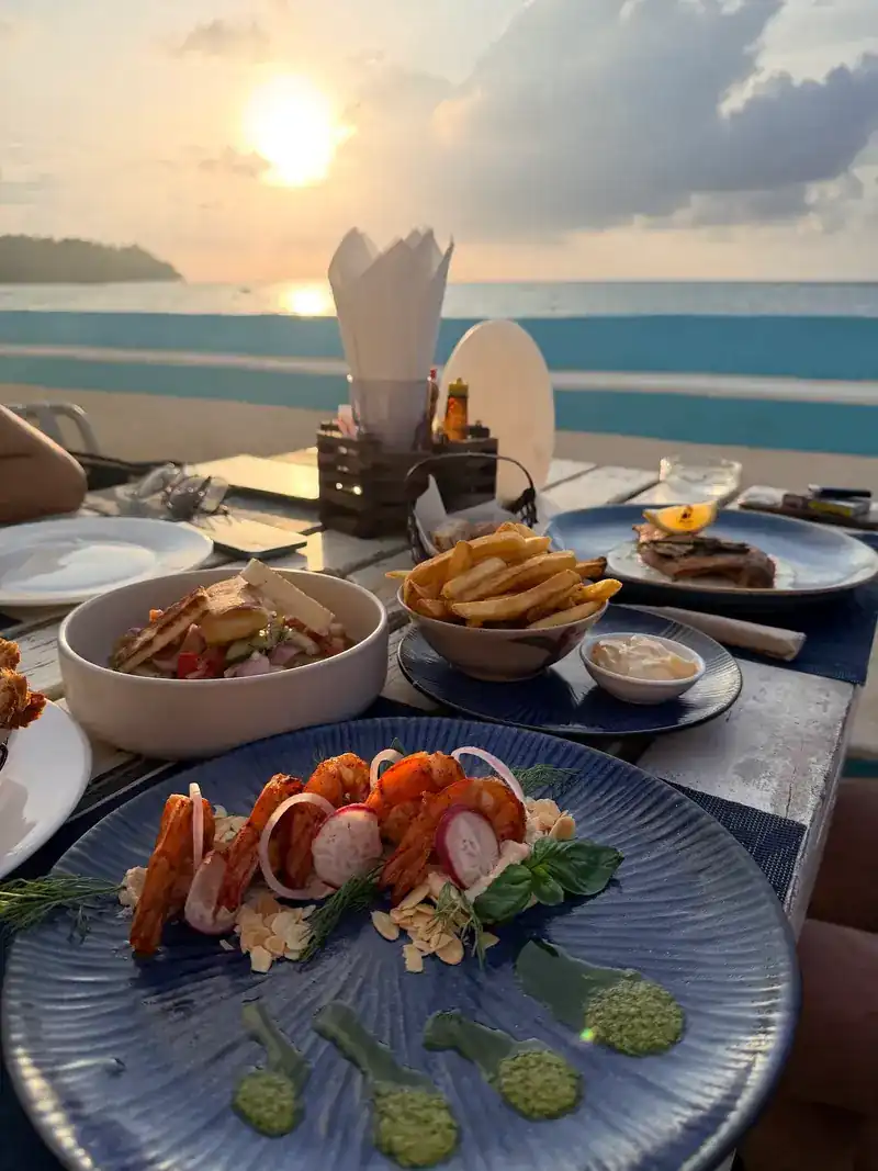 A plate of prawns with green sauce, the sun setting over the sea behind
