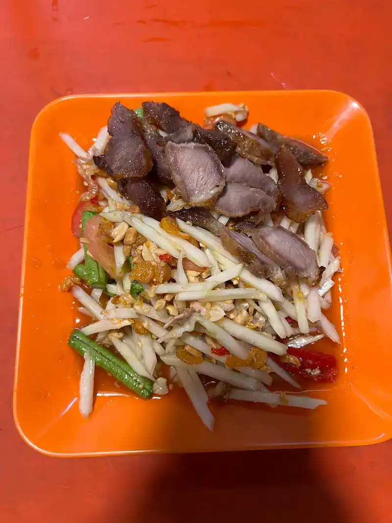 Papaya salad topped with sliced grilled pork neck on an orange plate / ส้มตำสันคอหมูย่างในจานสีส้ม