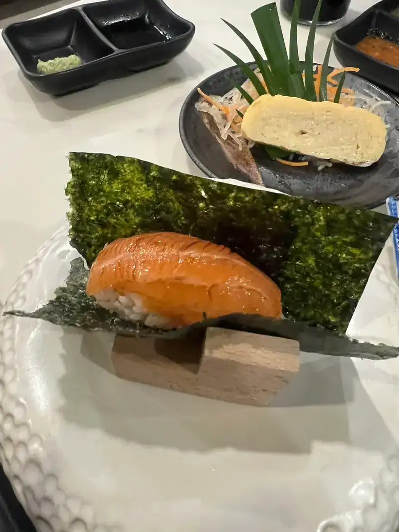 Salmon nigiri on a sheet of nori, with tamago behind