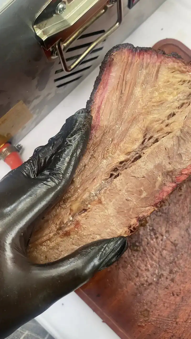 A gloved hand holding smoked brisket, a pink ring under the dark bark