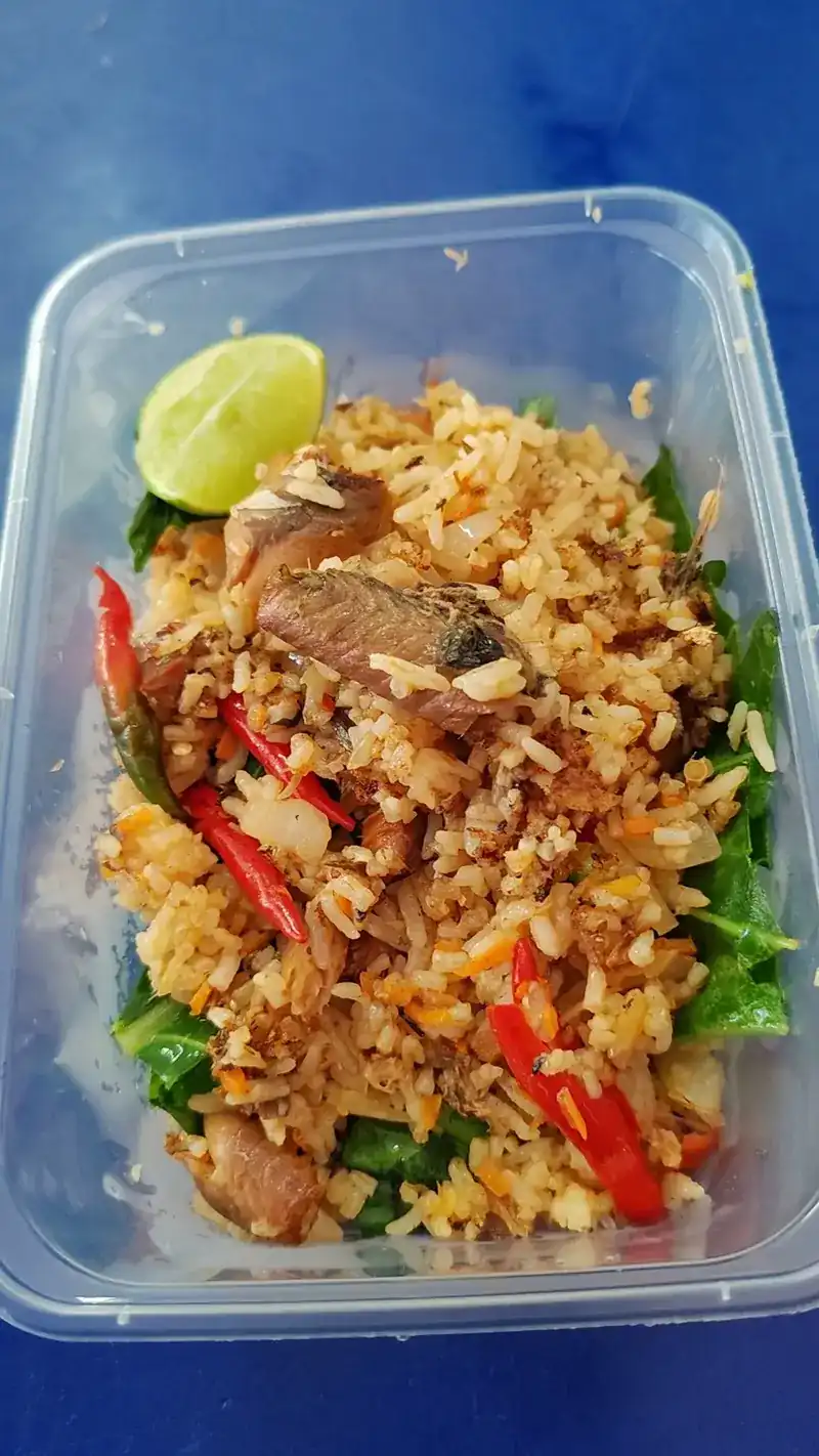 Fried rice with red chilli, greens and a lime wedge in a clear takeaway box on a blue table