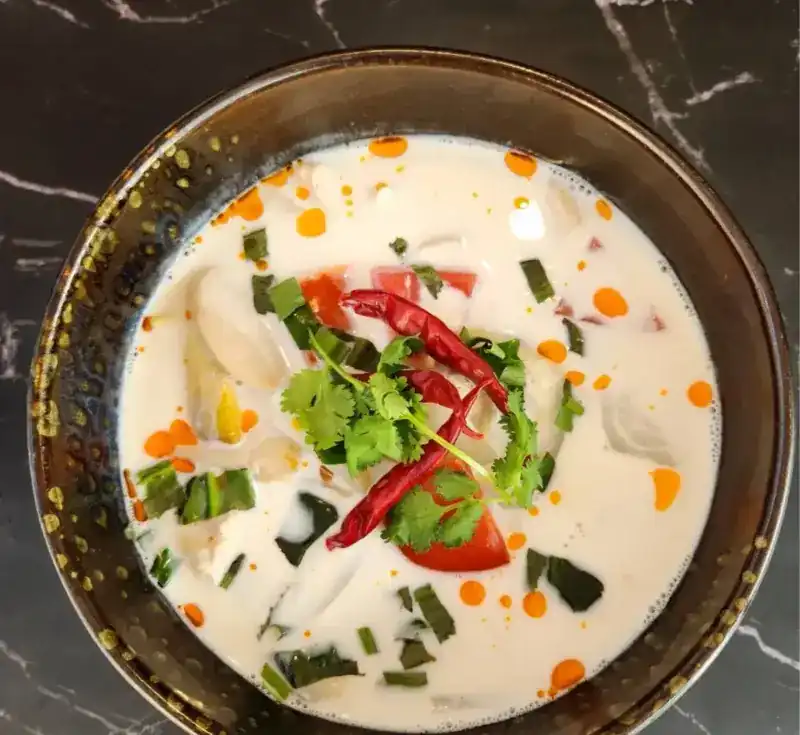 Tom Kha in a dark bowl with chillies and coriander