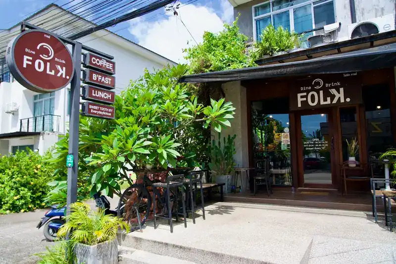 The shopfront on Srisoonthorn Road: the round Folk sign with its four boards, plants and tables by the door