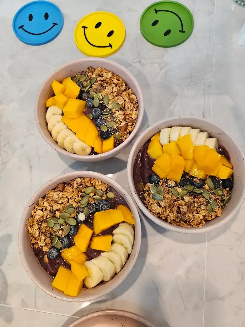 Three bowls topped with mango, banana, granola and seeds, next to smiley coasters