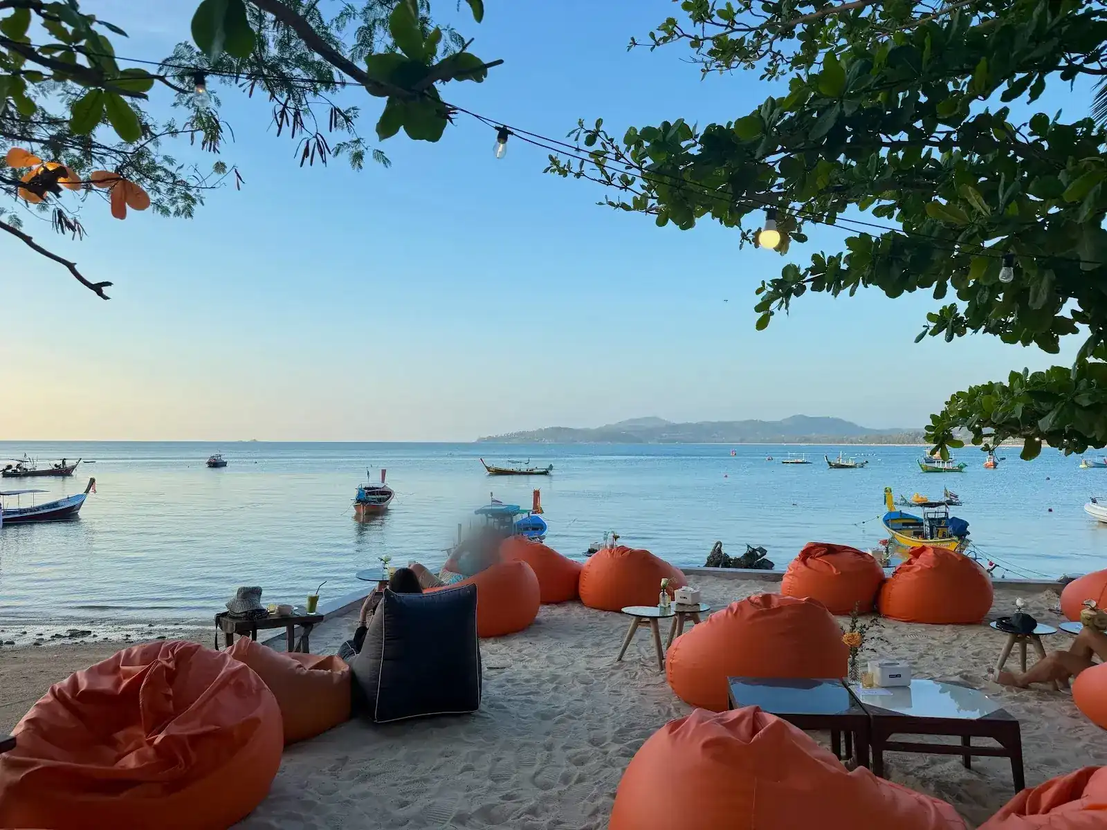 Orange bean bags on the sand facing Bang Tao bay, longtail boats moored in calm water