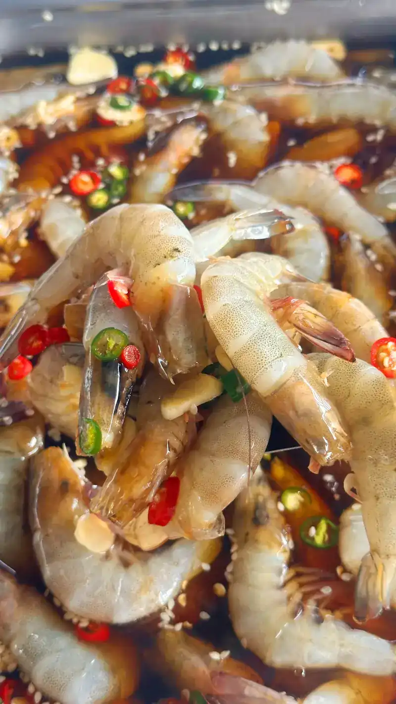 Raw prawns in a dark sauce with sliced chilli and garlic