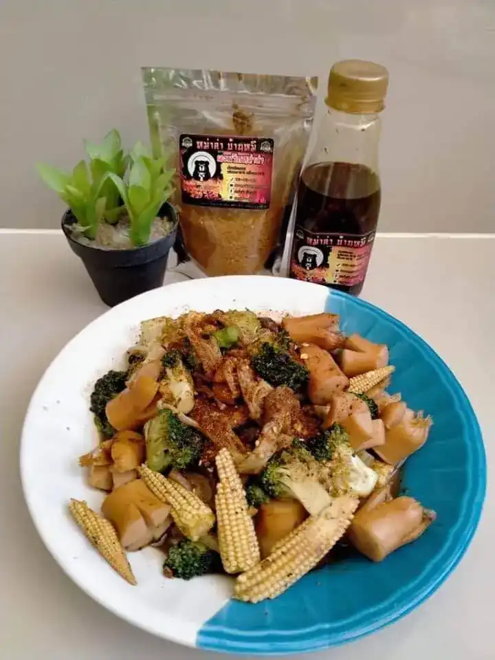 A plate of sausage, baby corn and broccoli tossed in mala, with a bag of mala powder and a bottle behind it