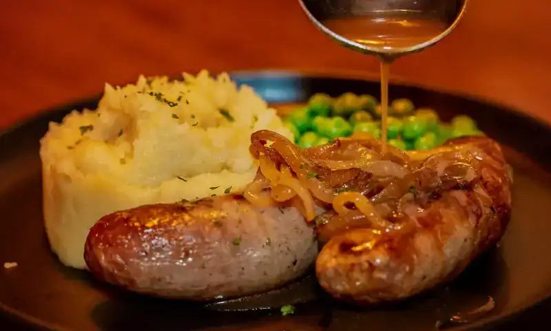 Sausages with mashed potato and peas, onion gravy being poured