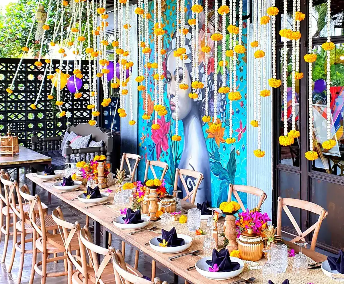 A long table set for a party under strings of marigolds, in front of a painted wall
