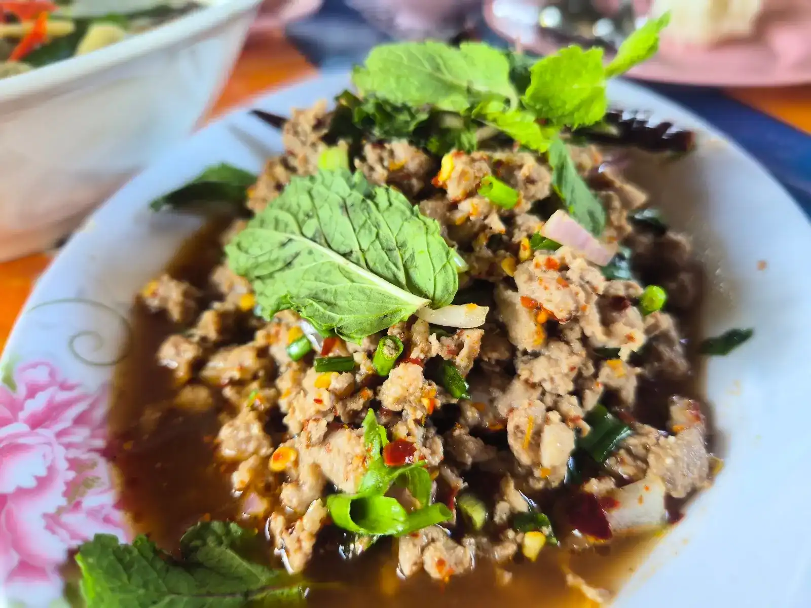 Larb with mint leaves, spring onion and chilli on a flower-painted plate