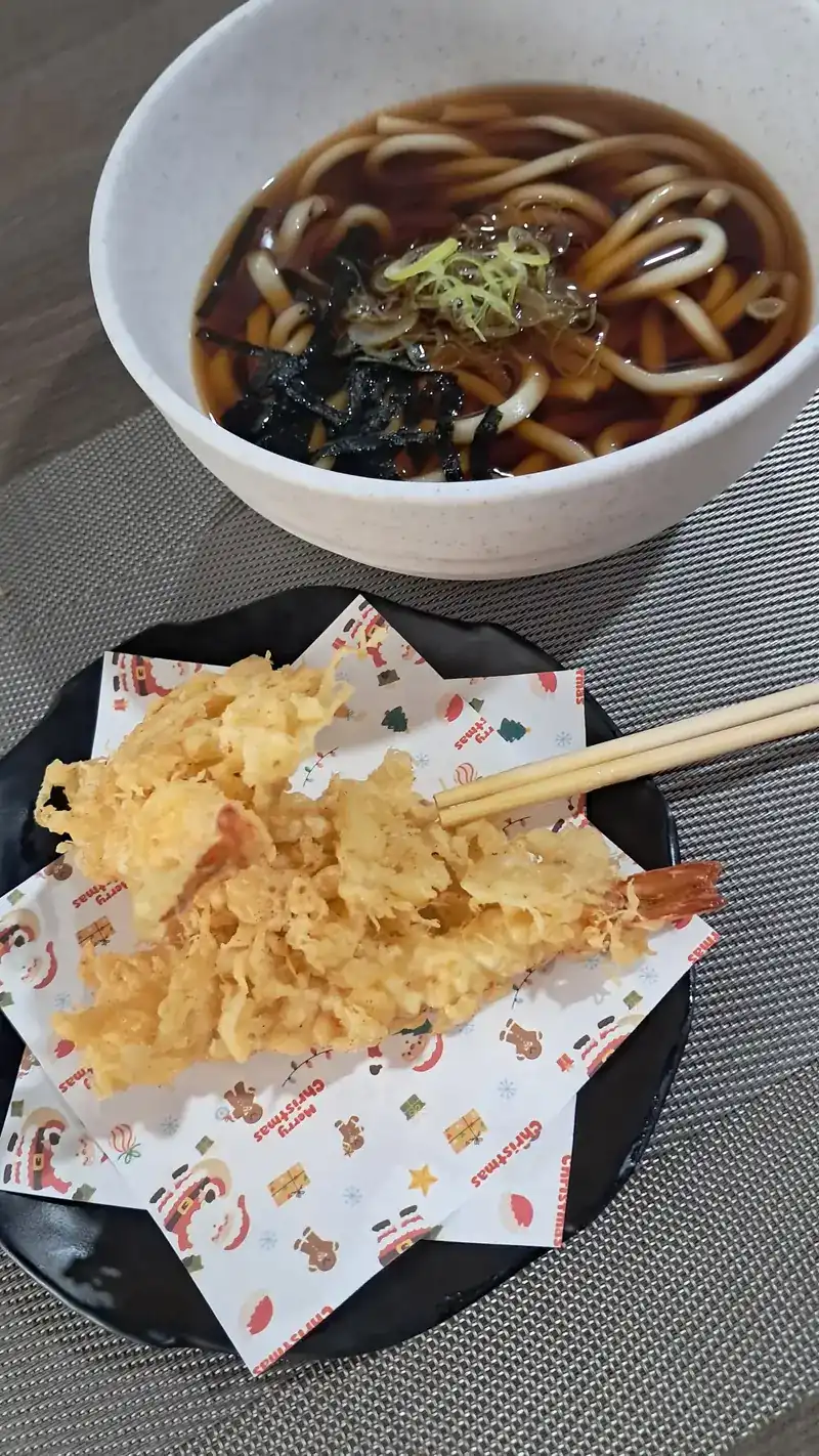 A bowl of udon in dark broth with seaweed and spring onion, and a plate of shrimp tempura