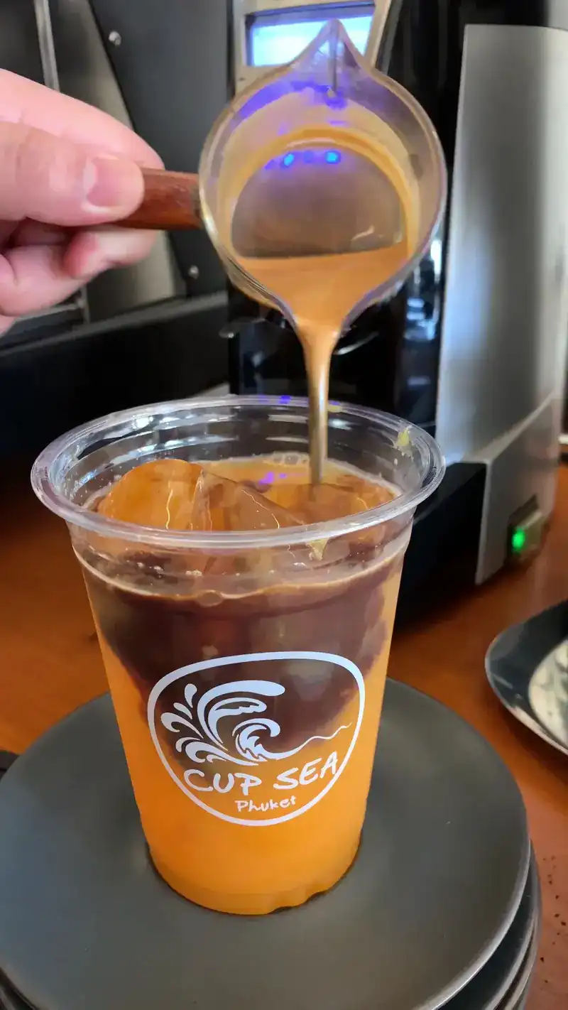 A barista pours espresso over an iced orange drink