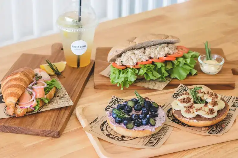A smoked salmon croissant, a tuna sandwich and two bagels topped with blueberries and banana