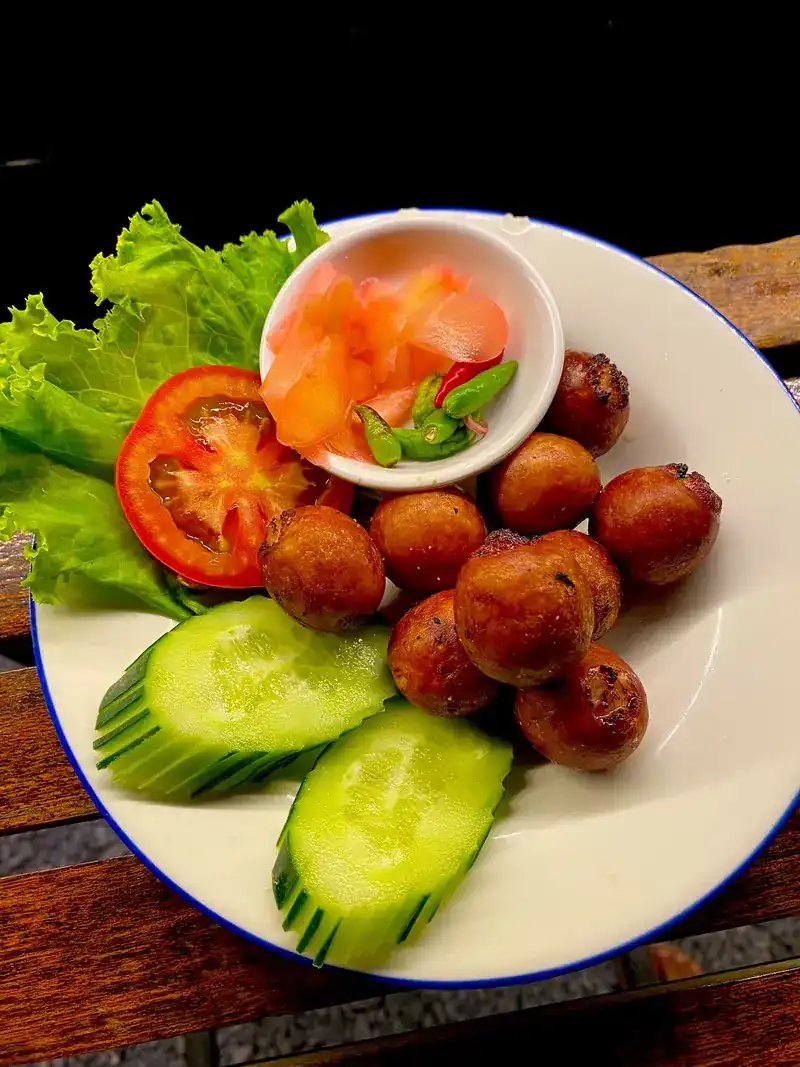 Isan sausages on a plate with cucumber, tomato, lettuce and chillies
