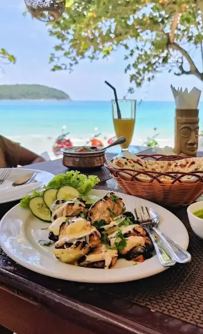 Grilled chicken, naan and green chutney on a table facing the beach