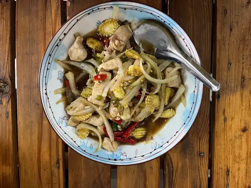 Chicken stir-fried with baby corn, onion and chilli in a white bowl, seen from above on wooden slats