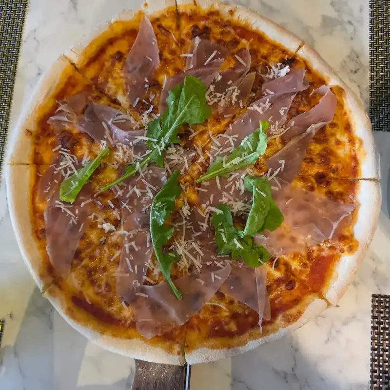 A thin-crust pizza topped with cured ham, rocket and grated cheese