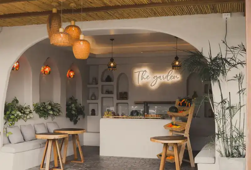 The counter under a glowing sign, with woven lamps, wooden stools and potted plants