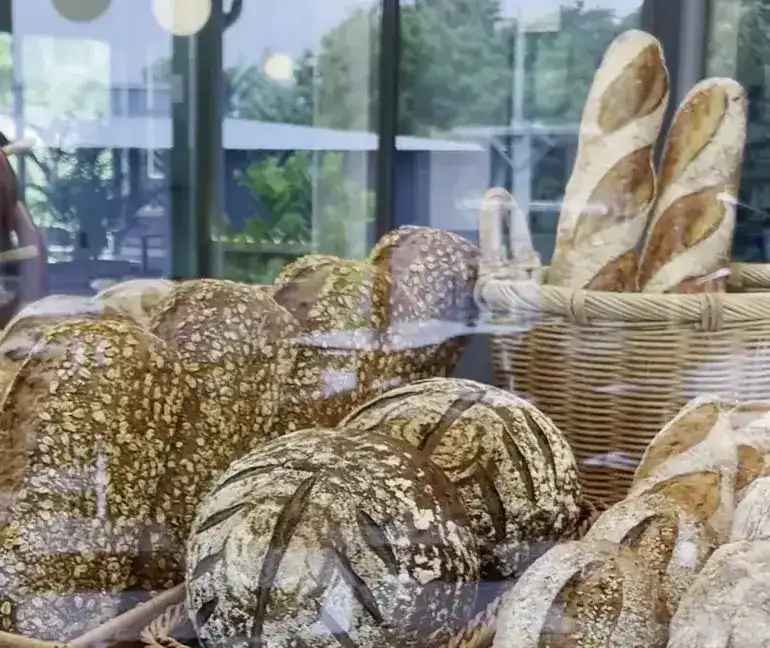Seeded loaves, country breads and baguettes in wicker baskets behind the glass counter