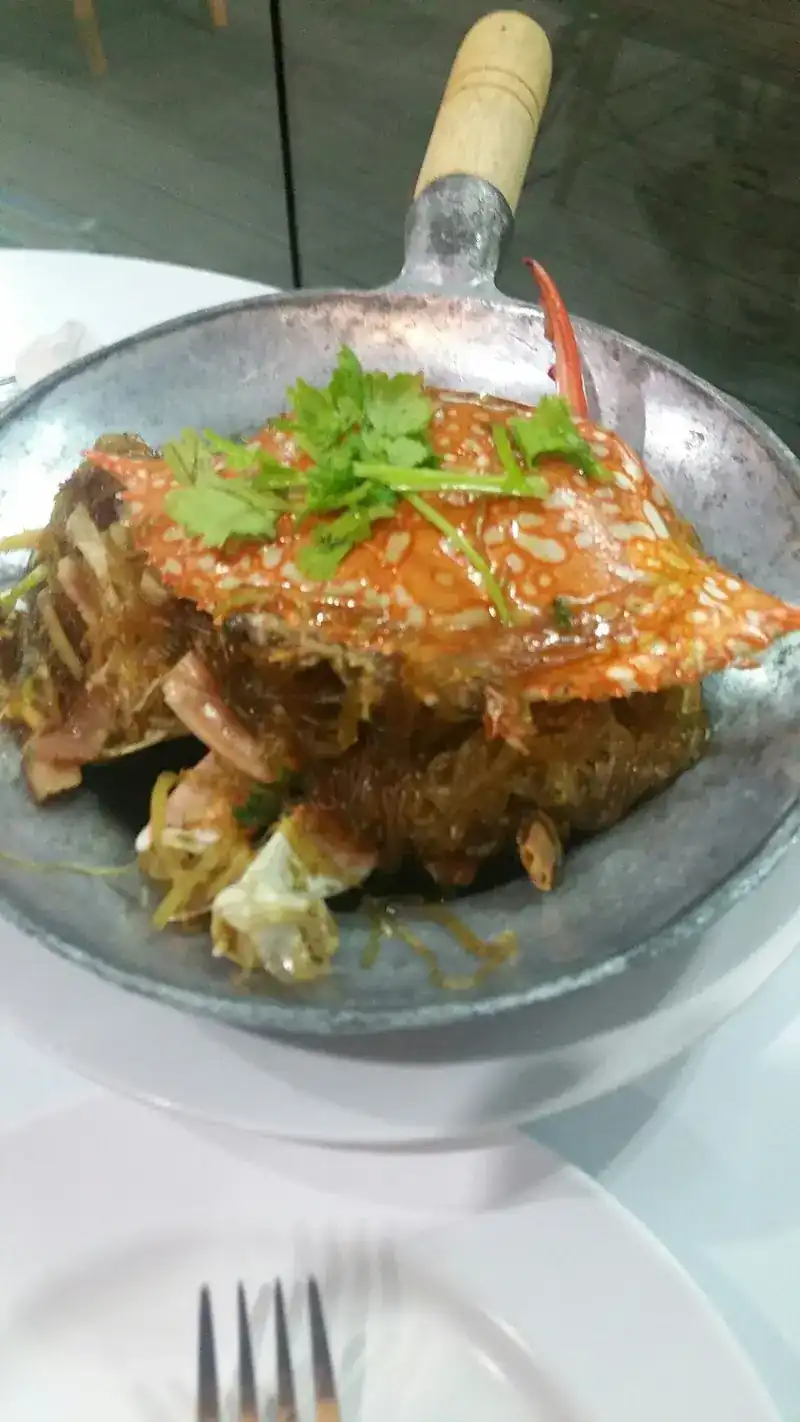 A crab shell on top of glass noodles in a metal pan with a wooden handle