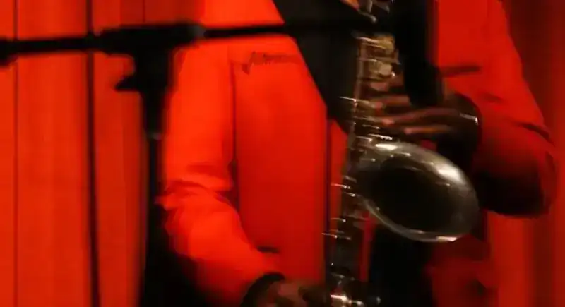 A saxophonist in a red jacket in front of the stage curtain