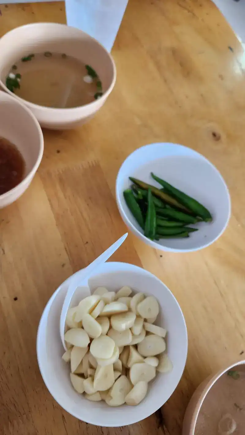 Small bowls of raw garlic and green chillies next to a bowl of soup on a wooden table