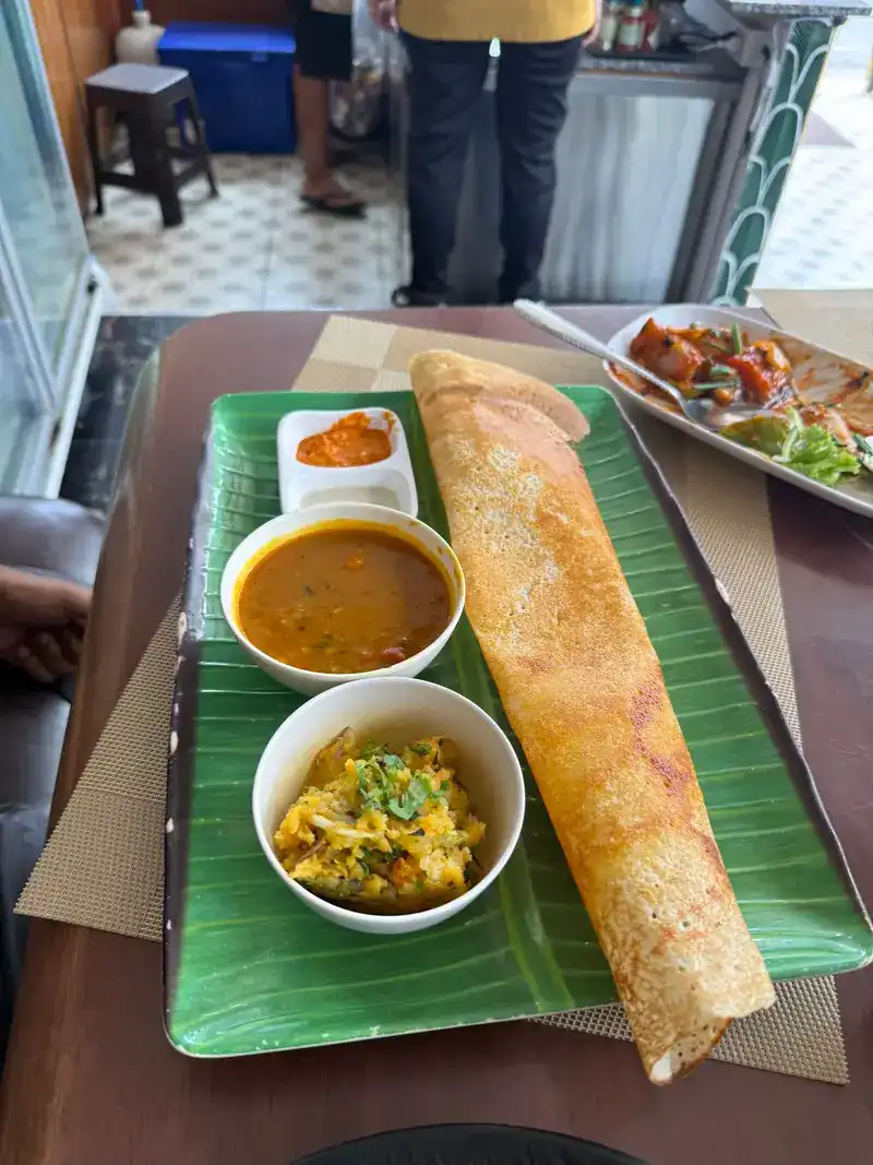 A long golden dosa on a leaf-green tray with sambar, potato masala and chutney