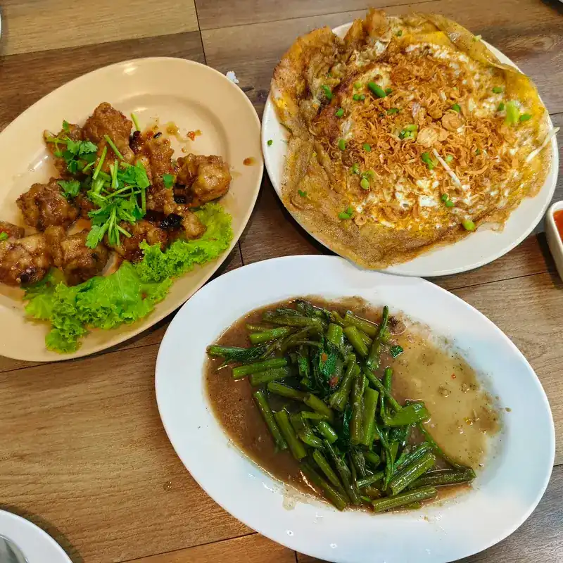 Oyster omelette with crispy shallots, a fried dish with coriander, and stir-fried morning glory on a wooden table