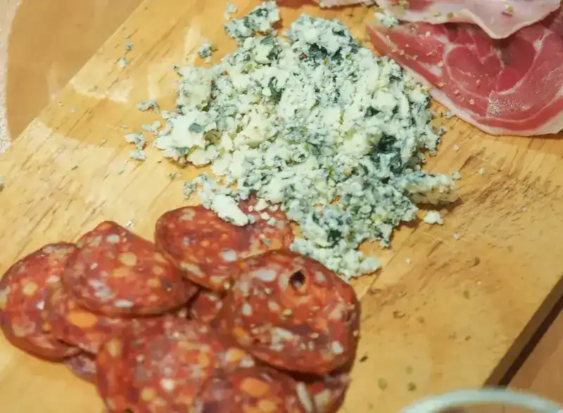 Sliced salami, crumbled blue cheese and cured ham on a wooden board