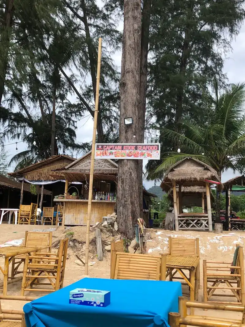 The Captain Kook Seafood sign on a tree above thatched huts and bamboo chairs