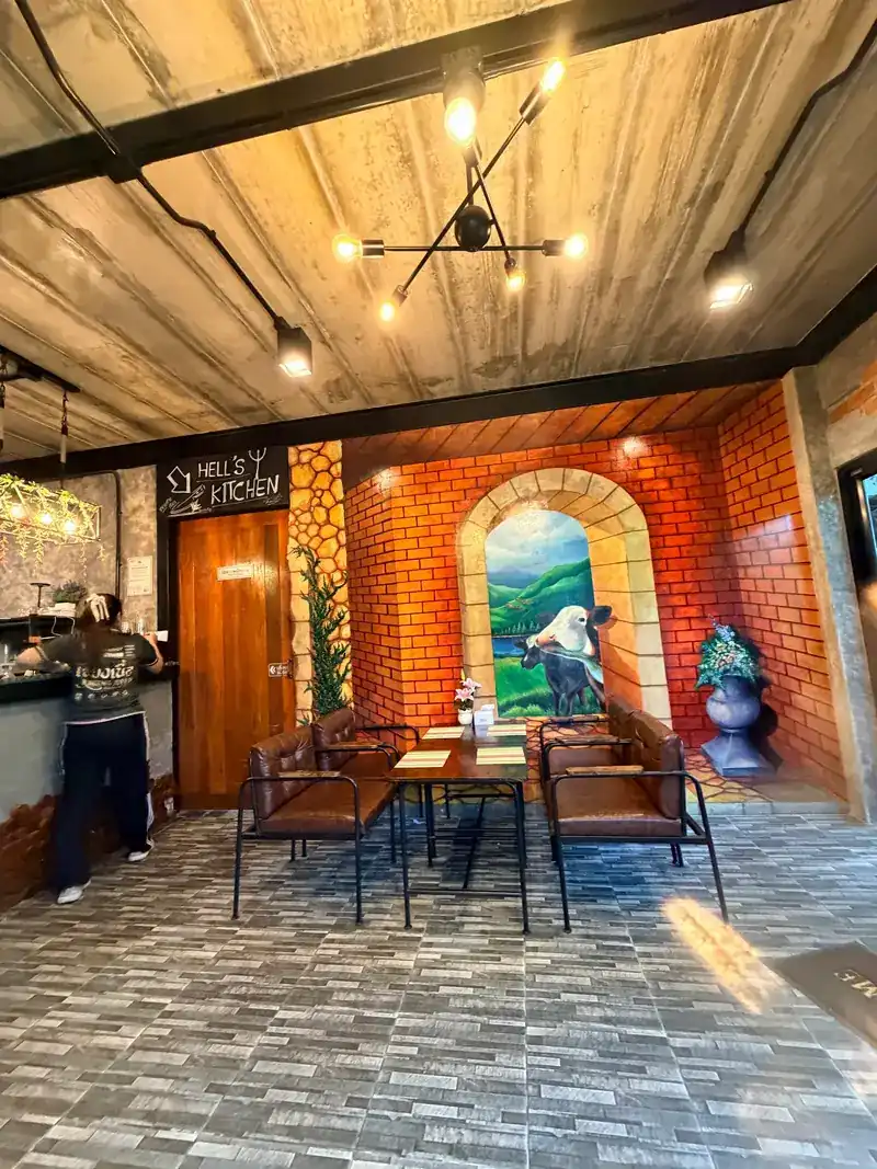 The dining room: leather chairs, a bare concrete ceiling and a brick wall painted with cows in a meadow