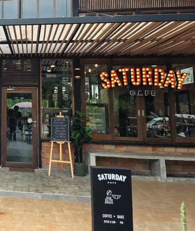 The front of Saturday Cafe: the marquee-bulb sign in the window, a chalkboard easel and the Coffee + Bake board under the timber pergola