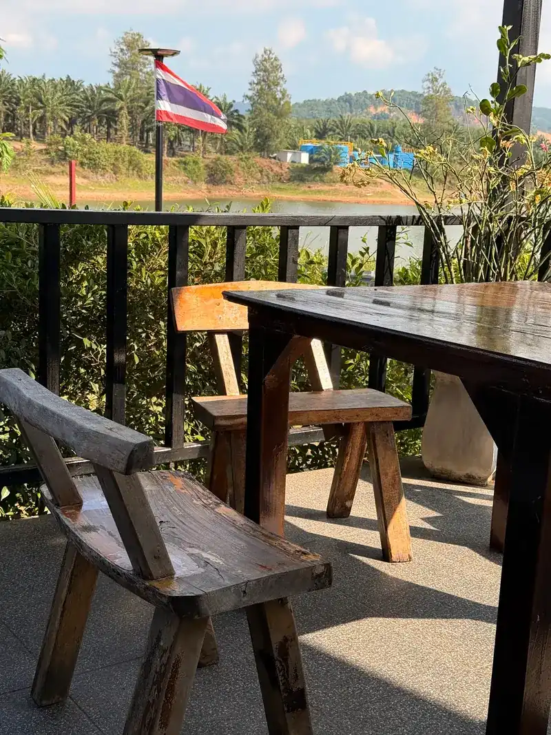 Wooden table and benches on the terrace, with a Thai flag, water and wooded hills beyond