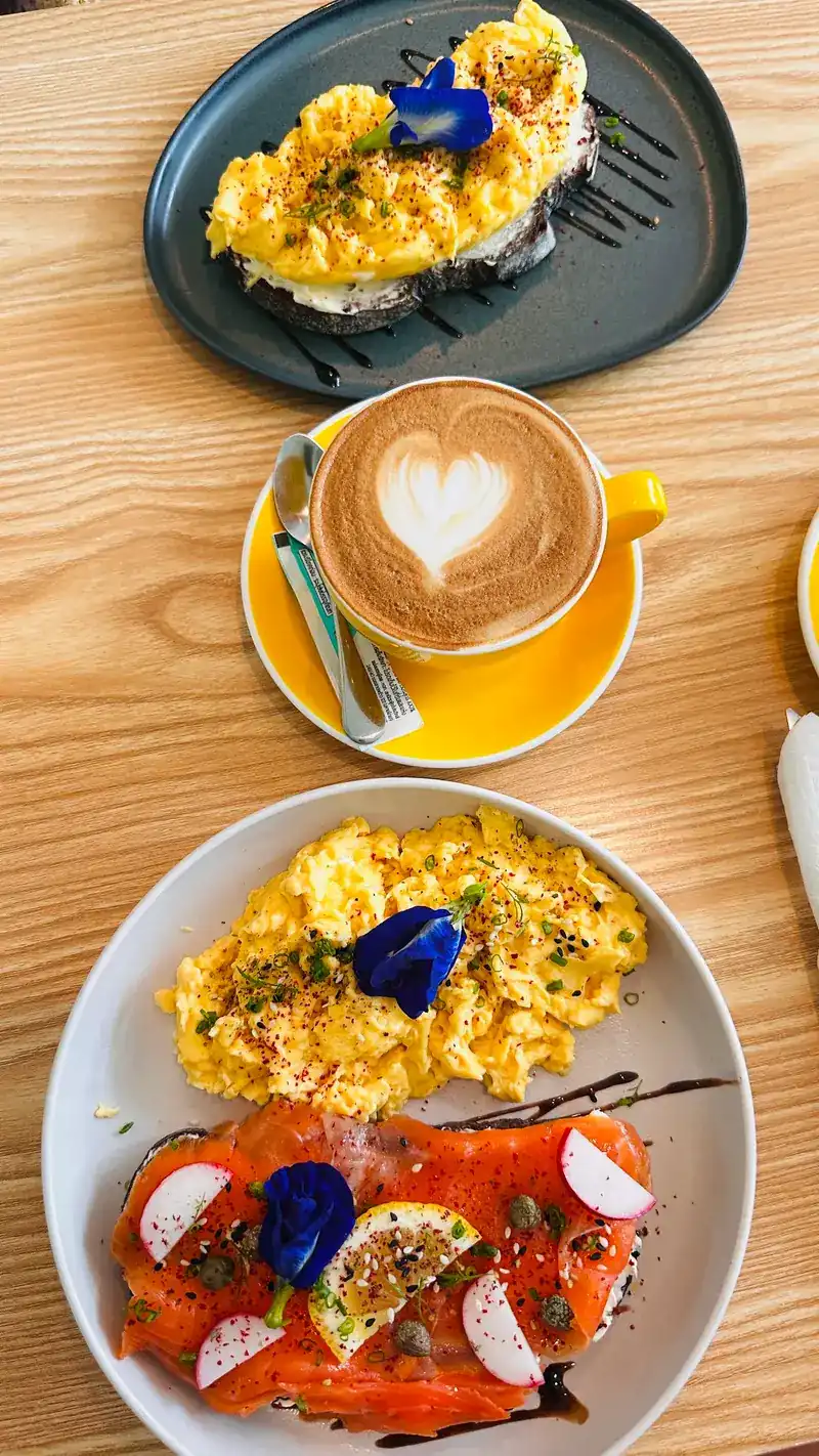 Scrambled eggs on toast, a latte with a heart and smoked salmon toast on a wooden table