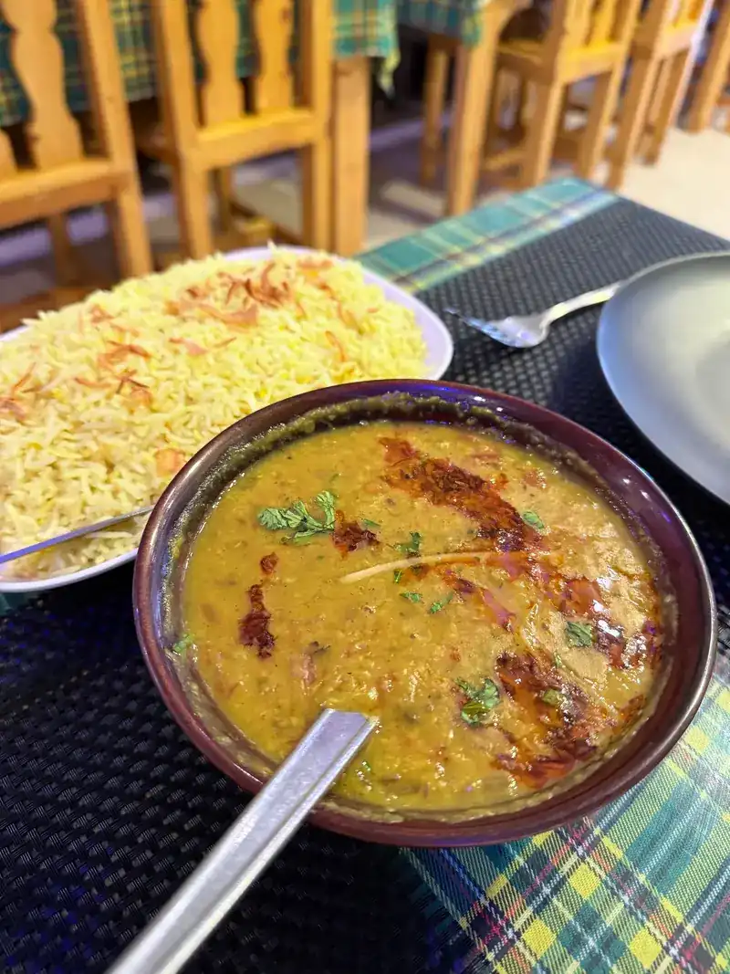 A bowl of yellow dal beside a plate of rice on a check tablecloth